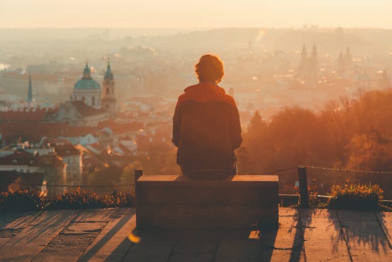 A person sitting quietly on a bench overlooking a calm landscape, symbolizing reflection and pause.