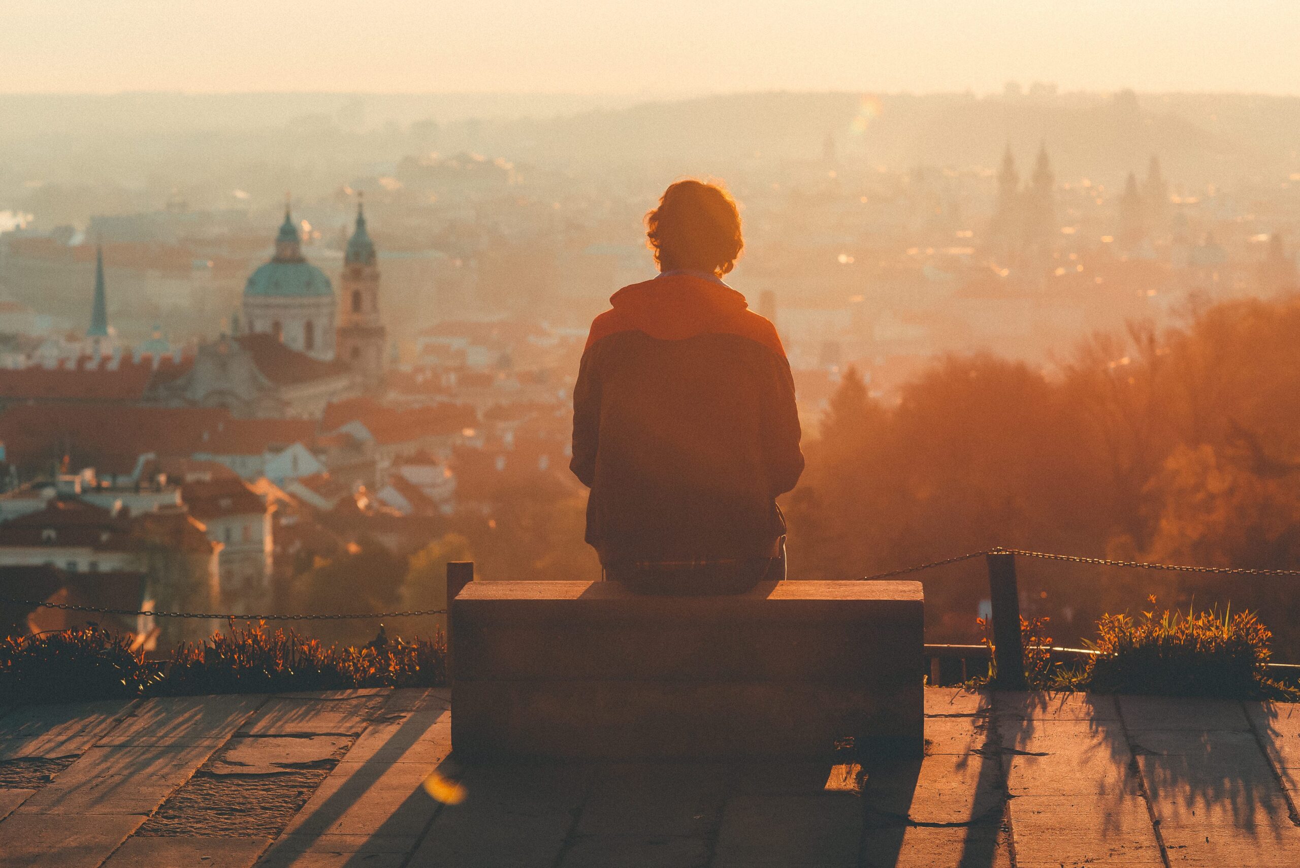 A person sitting quietly on a bench overlooking a calm landscape, symbolizing reflection and pause.
